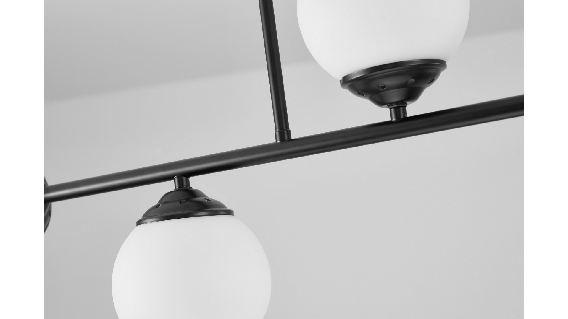 Lampa wisząca z czterema białymi kloszami, połączonymi czarnym stelażem, nowoczesny design z eleganckim akcentem czerni.