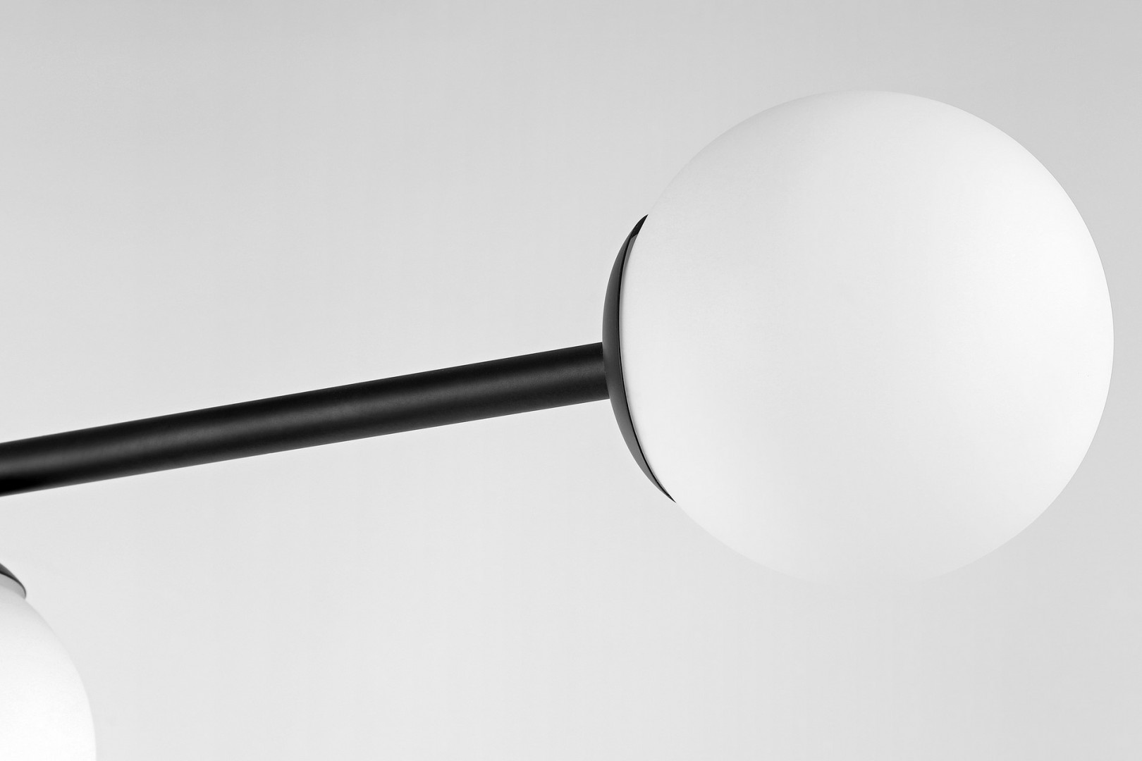 Detal matowobiałego klosza i czarnej oprawy nowoczesnej lampy sufitowej w stylu minimalistycznym.