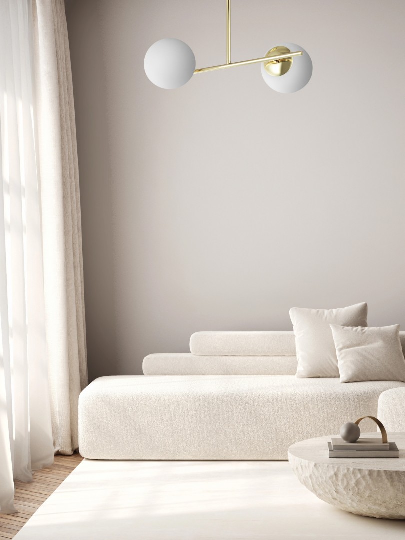 Złota nowoczesna lampa wisząca z dwoma mlecznobiałymi kloszami w minimalistycznym, jasnym salonie w stylu modern i japandi.