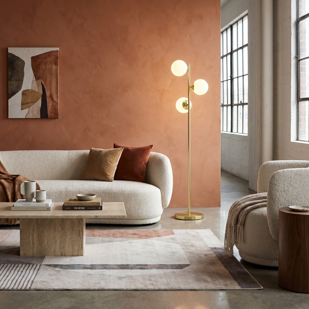 Lampa podłogowa FINO W3 marki Lampit w złotej odsłonie idealnie wpisuje się w nowoczesny salon z beżową sofą