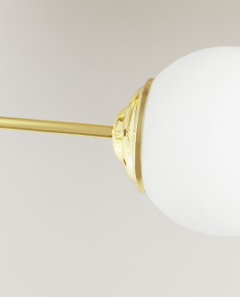 Detal złotej lampy z matowym, mlecznobiałym kloszem kulistym na metalowym ramieniu