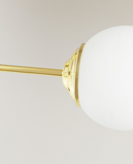 Detal złotej lampy z matowym, mlecznobiałym kloszem kulistym na metalowym ramieniu