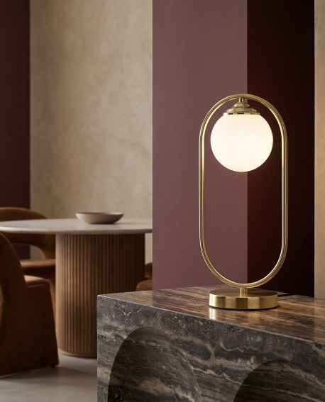 Złota lampa biurkowa VERO ustawiona w eleganckim wnętrzu z ciemnymi detalami
