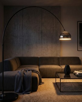 Czarno-chromowana lampa łukowa oświetla salon wieczorem nad sofą