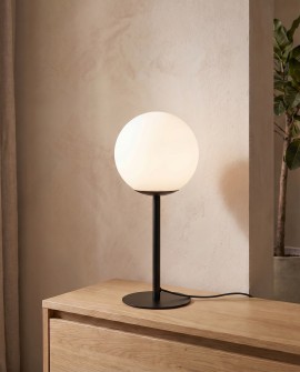 Lampa stołowa o czarnej podstawie i białej kuli ustawiona na komodzie
