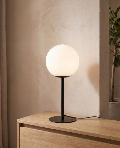 Lampa stołowa o czarnej podstawie i białej kuli ustawiona na komodzie